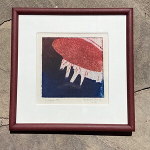May include: Framed abstract print titled "Eclipse #4" with a red and white shape over a dark blue background. The print is in a white mat and a burgundy frame. The artist's signature and date are visible.