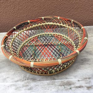 May include: A woven basket with a circular shape and a colorful design. The basket is made of natural materials and has a unique, hand-crafted look.