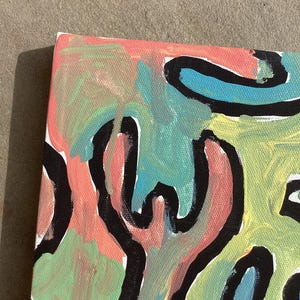 Puede incluir: Pintura abstracta sobre lienzo con superficie texturizada. La obra presenta una vibrante mezcla de colores, incluyendo coral, azul claro y verde, con contornos negros audaces. La composici&oacute;n es una vista de cerca de la esquina del lienzo.