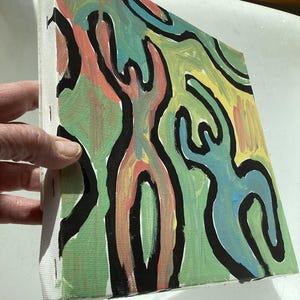 Puede incluir: Lienzo de arte abstracto con formas coloridas delineadas en negro. La obra de arte presenta figuras en tonos verdes, amarillos, azules y coral. El lienzo est&aacute; estirado y grapado a un marco de madera, listo para exhibir. La pintura est&aacute; sostenida por una mano.