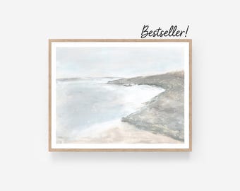 May include: A framed landscape art print featuring a coastal scene with a light blue sky and water, and a sandy beach. The artwork is in a wooden frame. The text "Bestseller!" is in the upper right corner.