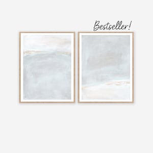 Puede incluir: Dos impresiones artísticas abstractas enmarcadas. Cada impresión presenta una paleta de colores suaves y apagados de azul claro, beige y dorado. La obra de arte tiene una calidad texturizada y pictórica. Los marcos son de color madera clara. El texto "Bestseller!" está escrito en cursiva.