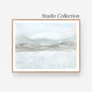 May include: A framed landscape art print with a minimalist design. The artwork features a soft color palette of light blue, gray, and beige, depicting a serene mountain scene. The words "Studio Collection" are printed at the top.
