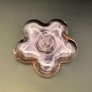 May include: A clear glass flower-shaped dish with a purple hue and a swirl pattern. The dish has five points and a small hole in the centre.