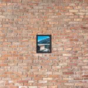 Puede incluir: Una fotograf&iacute;a enmarcada de un lago con un peque&ntilde;o edificio en la orilla. El lago est&aacute; rodeado de monta&ntilde;as cubiertas de nieve. El marco es negro y la foto es en color.