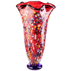Può includere: Un vaso in vetro alto e svasato con un colore di base rosso vibrante, arricchito da un denso motivo millefiori multicolore composto da piccole forme circolari e geometriche. Il vaso presenta un bordo ampio e ondulato e una base circolare blu scuro.
