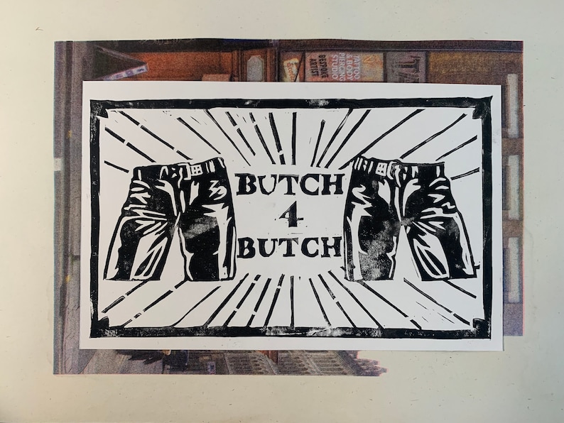 May include: A black and white print with the text "BUTCH 4 BUTCH" and two pairs of jeans. The design incorporates radiating lines, creating a striking graphic. The image is set against a backdrop of a street scene.