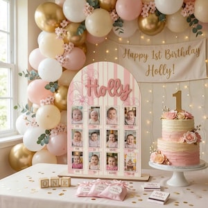 May include: A first birthday party scene with a cake, balloons, and a photo display. The cake is two-tiered with pink frosting and floral decorations. A banner reads "Happy 1st Birthday Holly!" and a wooden sign displays photos.