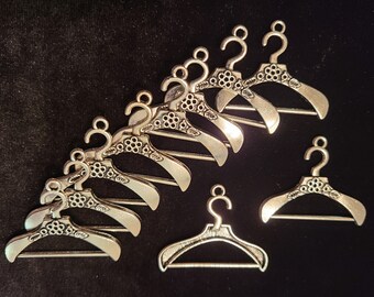 May include: A set of ten silver-toned miniature hangers with decorative floral details. The hangers are arranged in a semi-circle on a black background.