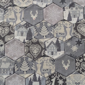 May include: A collection of hexagonal fabric tiles with a winter holiday theme. The tiles feature various patterns, including reindeer, houses, snowflakes, and hearts, in shades of grey, white, and cream. The overall design creates a patchwork effect.