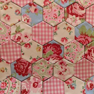 May include: A collection of fabric hexagons arranged in a repeating pattern. The individual pieces feature various prints including pink and white gingham checks, red roses on cream backgrounds, and intricate floral designs in shades of pink and blue.