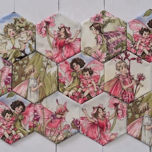 May include: A collection of ten hexagonal fabric patches featuring detailed illustrations of fairies with pink and green wings, surrounded by flowers and foliage. Each patch displays a unique scene of winged figures in various poses among blossoms.