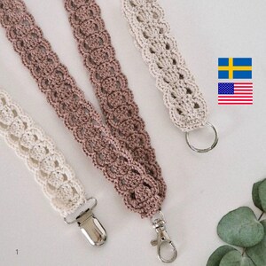 Op de afbeelding: Close-up van drie gehaakte lanyards in cr&egrave;me, mauve en beige. Elke lanyard heeft een decoratief openwerkpatroon en is afgewerkt met een metalen sluiting of ring. De lanyards worden getoond tegen een lichte achtergrond.