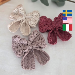 May include: Three handmade crochet bows in shades of beige, mauve, and burgundy. The bows have a textured, floral-like pattern on the center and the loops. The bows are arranged on a light-colored surface, showcasing their delicate craftsmanship.