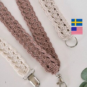 Op de afbeelding: Close-up van drie gehaakte lanyards in cr&egrave;me, mauve en beige. Elke lanyard heeft een decoratief openwerkpatroon en is afgewerkt met een metalen sluiting of ring. De lanyards worden gepresenteerd tegen een zachte, neutrale achtergrond.