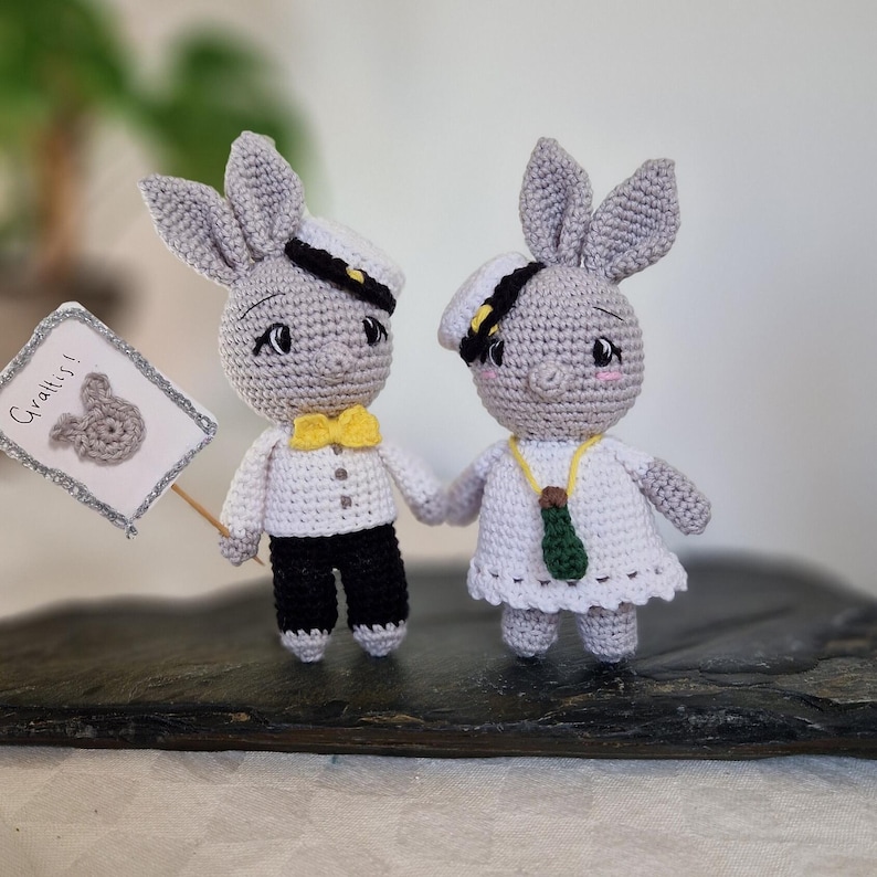 May include: Two crocheted bunny figurines dressed in sailor outfits. One bunny holds a sign that says "Grattis!" which is Swedish for "Congratulations!"