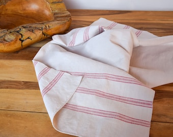 May include: A white linen kitchen towel with red stripes. The towel is folded and lying on a wooden surface.