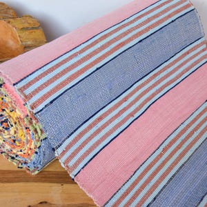 Peut inclure: Un tapis rayé rose et bleu roulé avec une texture tissée. Le tapis est roulé et le bout du rouleau est visible, montrant les différentes couleurs du tapis.