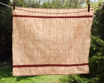 May include: A beige linen tea towel with a red trim. The towel is hanging on a clothesline.
