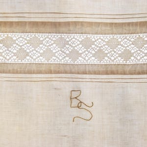May include: A white linen fabric with a brown lace trim and a brown embroidered letter "R" in the center.