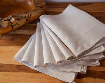 May include: A stack of eight off-white linen tea towels folded neatly on a wooden surface.