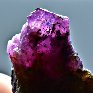 Könnte beinhalten: Ein großer, rauer, violetter Edelstein mit kristalliner Struktur. Der Edelstein ist undurchsichtig und hat eine tiefe, satte violette Farbe.