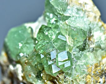 May include: A cluster of green grossular garnet crystals in a matrix of white rock. The crystals are translucent and have a glassy luster.