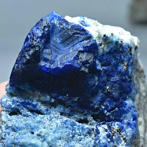 Może przedstawiać: Zbliżenie na niebieski okaz mineralny o szorstkiej, krystalicznej strukturze. Minerał jest osadzony w macierzy białej i szarej skały.