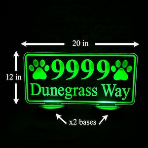 May include: Green illuminated acrylic house number sign with paw prints and the text "9999 Dunegrass Way". The sign is 20 inches wide and 12 inches tall and has two bases.
