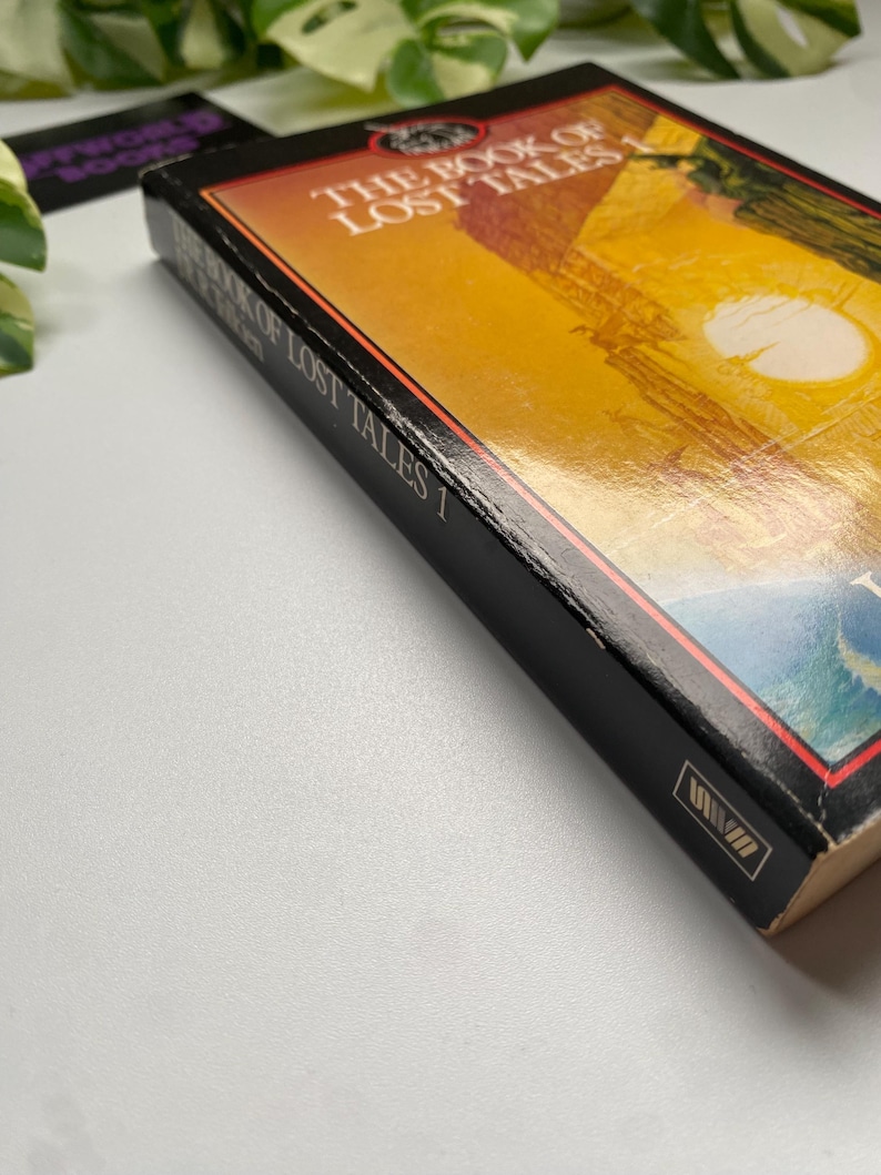 K&ouml;nnte beinhalten: Ein Hardcover-Buch mit dem Titel "The Book of Lost Tales 1" mit schwarzem Buchr&uuml;cken und einem farbenfrohen Cover mit einer Landschaftsszene mit Sonne. Das Cover des Buches hat einen Farbverlauf von Orange und Gelb.