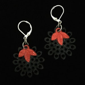 以下が含まれることがあります： 繊細なレースのデザインと赤い葉のアクセントが付いた、黒と赤のイヤリングのペアです。