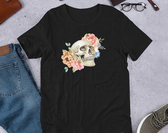 May include: Black t-shirt featuring a watercolor design of a skull adorned with pink, peach, and blue flowers. The shirt is made of a soft material and has a classic crew neck design. A casual and artistic apparel item.