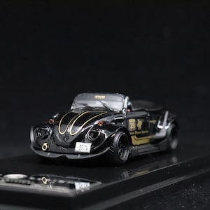 May include: A black convertible toy car with gold accents and a license plate. The car has a low profile, black wheels, and a detailed interior. The car has a gold emblem on the side and a black background.