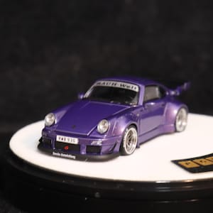 May include: A purple model car with a spoiler and silver wheels. The car has the text "RAUH-Welt" on the windshield and "RWB 930" on the front. The car is on a white platform.