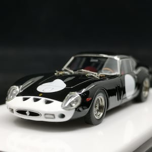 以下が含まれることがあります： 白と黒のモデルカー。白いレーシングストライプとドアの白い円が特徴です。車は白いフロントエンドとシルバーのホイールを備えています。白い表面に置かれています。