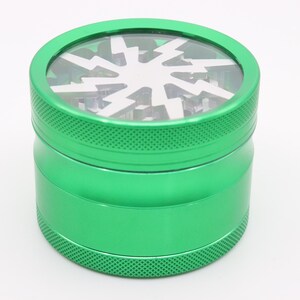 Peut inclure: Un broyeur cylindrique vert avec un dessus transparent orné d'un motif d'éclair blanc. Le corps en métal présente une texture antidérapante sur les bords supérieur et inférieur. Idéal pour les herbes.