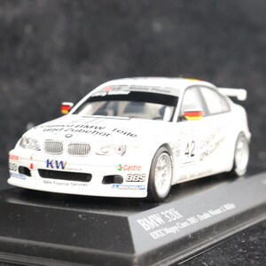 May include: A white BMW 320i race car model with German flag accents. The model features the number 42 and sponsor logos. It sits on a black display base, showcasing a detailed replica of a racing vehicle.