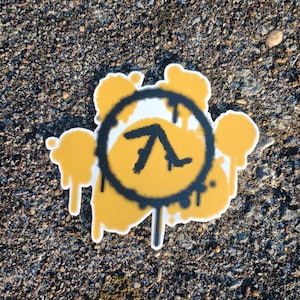 Puede incluir: Una pegatina amarilla y negra pintada con aerosol con un símbolo lambda dentro de un círculo. La pegatina tiene un efecto de goteo alrededor de los bordes.