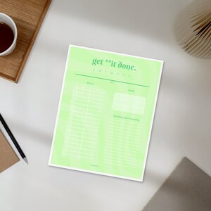 May include: A light green planner sheet with the text "get **it done." is on a white surface. A cup of tea, a notepad, and a pen are next to the planner. The planner has sections for tasks and priorities.