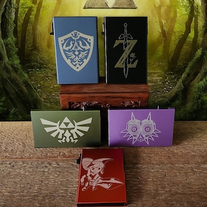 May include: Five metal card holders in various colors, each featuring a different design from a popular video game series. The colors include blue, black, green, purple, and red. The designs are etched in a contrasting color.