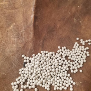 May include: A close-up of a pile of small, white, round beads on a brown wooden surface.