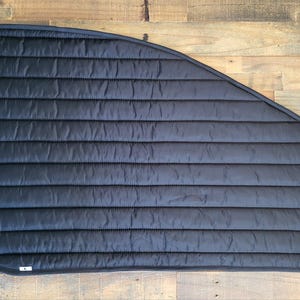 May include: Black quilted window shade for a car or van. The shade is curved to fit the shape of a window and has a black trim around the edges.