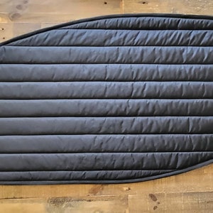 May include: Black quilted fabric panel with a curved edge and a small white logo in the corner. The panel has horizontal stitching creating a padded appearance. The item is likely a vehicle window cover or insulation.