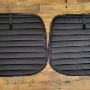 May include: Two black quilted window shades with a strap for hanging. The shades are designed to block out light and heat.
