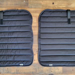 May include: Two black quilted window shades with a hook and loop fastener on each side. The shades are designed to block out light and heat.