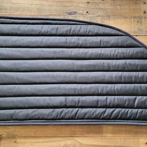 May include: Black quilted window shade for a car or van. The shade is curved to fit a side window and has a sewn edge.