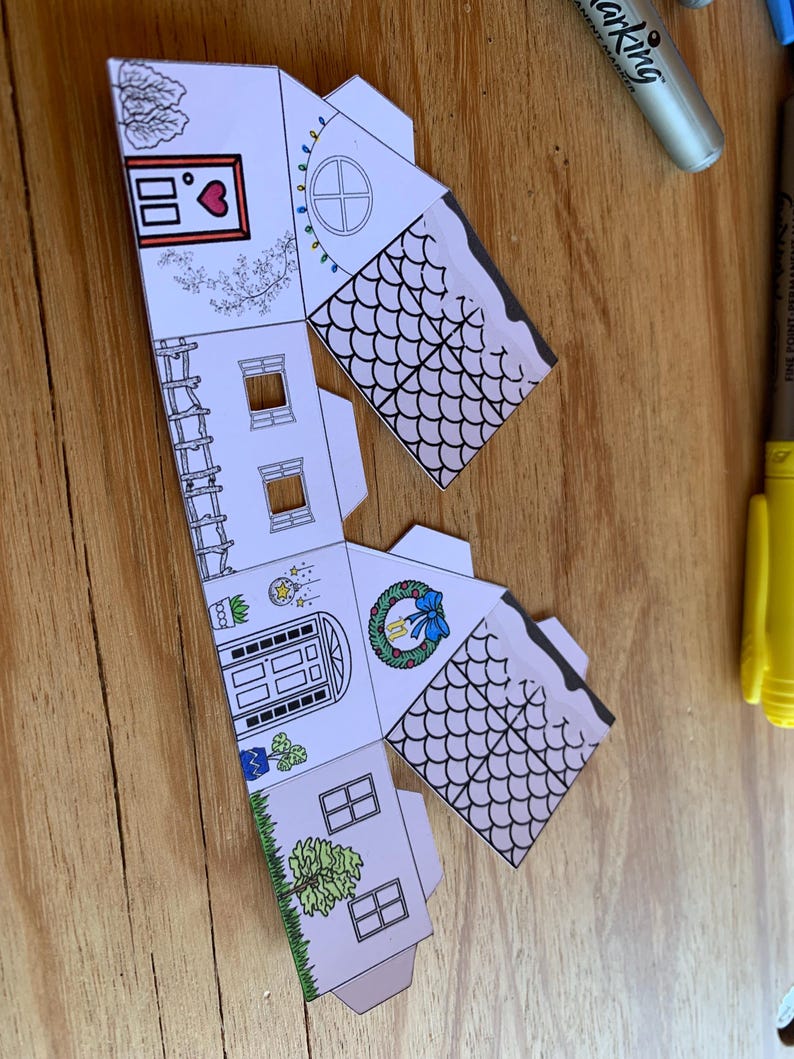 K&ouml;nnte beinhalten: Ein teilweise zusammengebautes Papierhaus mit detaillierten Illustrationen. Das Haus hat eine Eingangst&uuml;r, Fenster und ein Dach mit einem schuppenartigen Muster. Dekorationen umfassen einen Kranz, ein Herz und Lichterketten.