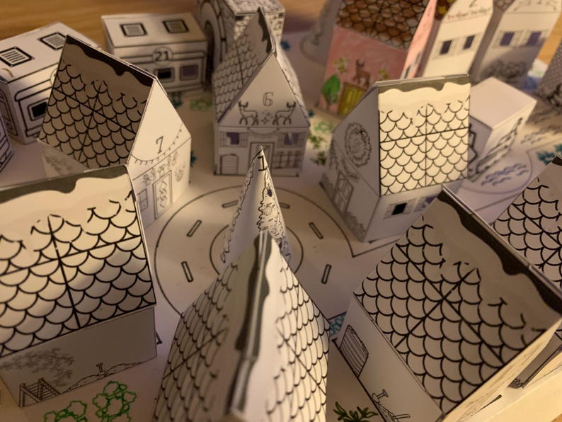 K&ouml;nnte beinhalten: Eine Sammlung kleiner Papierh&auml;user mit Schwarz-Wei&szlig;-Strichzeichnungen, die wie eine Stadt angeordnet sind. Einige H&auml;user haben Nummern und dekorative Details. Die D&auml;cher sind mit einem schuppenartigen Muster versehen, und die gesamte Szene befindet sich auf einer Papierbasis mit einer Stra&szlig;e.