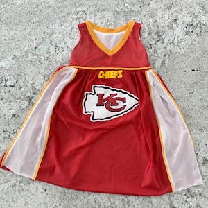 May include: A red and white dress with a Chiefs logo and the word "CHIEFS" in yellow. The dress has a V-neck and white mesh panels with yellow trim. The dress is sleeveless.