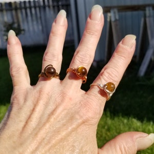 May include: Three wire-wrapped rings with tiger's eye stones. The rings are made with copper and silver wire. The stones are a golden brown color.